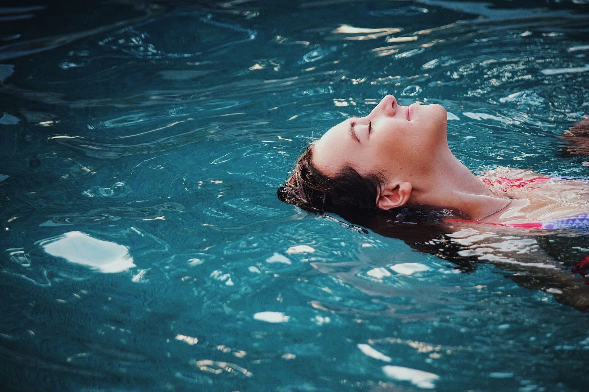 Femme flottant paisiblement dans une eau turquoise, visage apaisé.