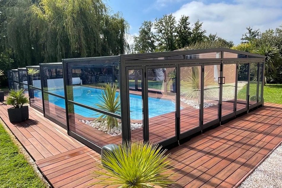Abri de piscine autour d'une piscine dans un jardin ensoleillé.